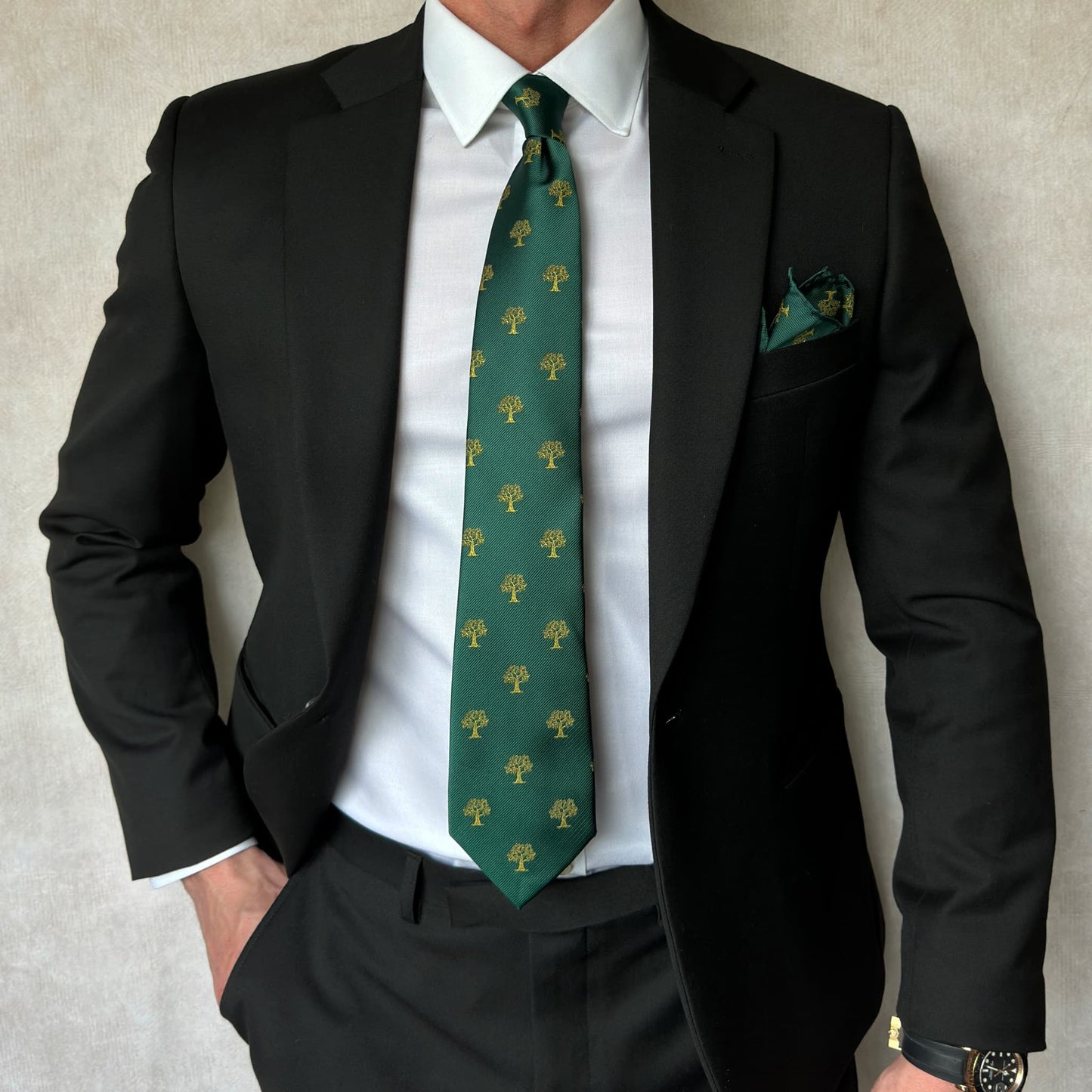 model wearing a black open suit and white shirt with green and gold tree necktie