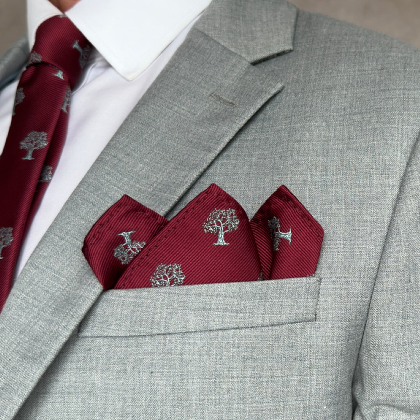 grey suit pocket showing off red pocket square emblazed with silver tree pattern
