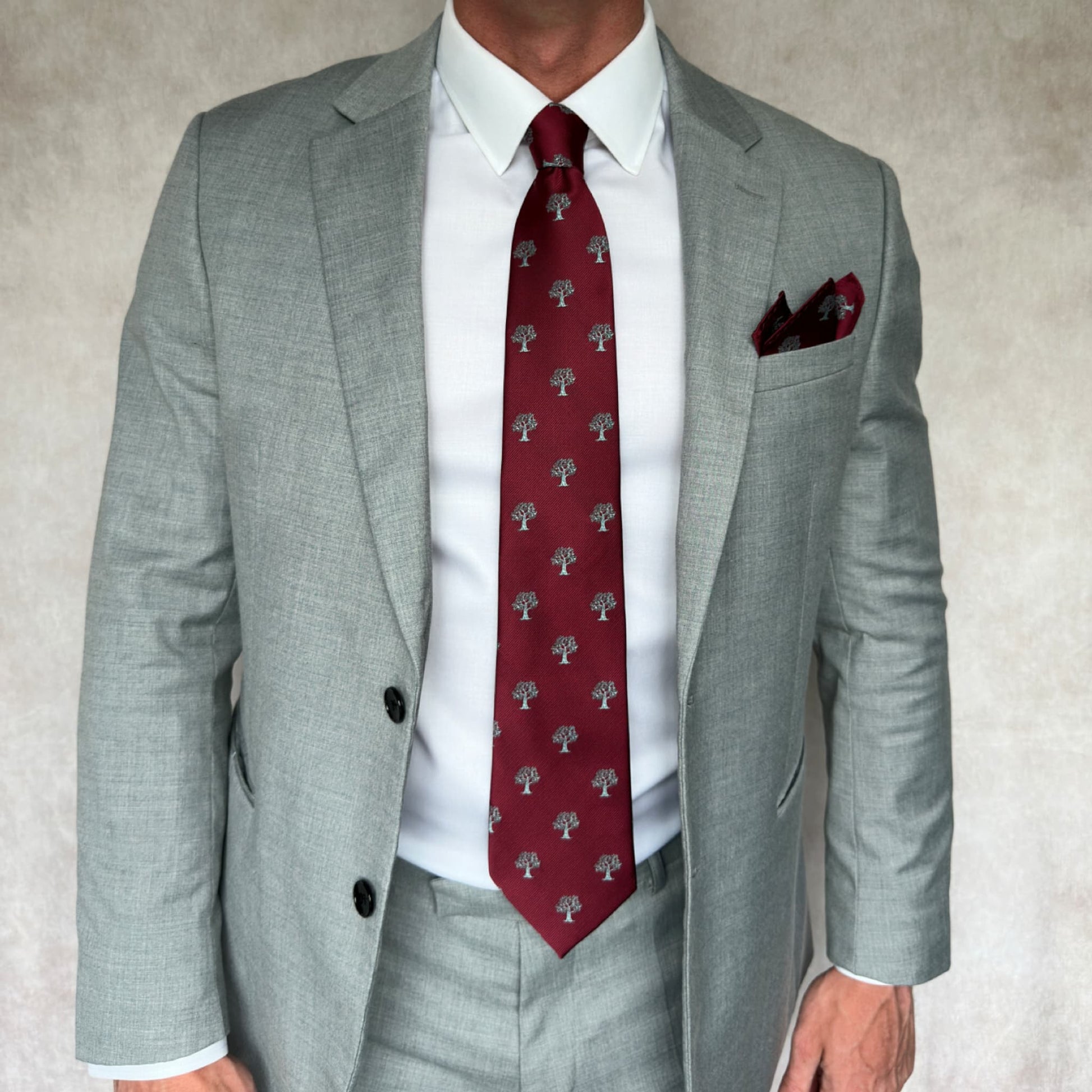 Model wearing grey suit showcasing matching red and silver tie and pocket square set