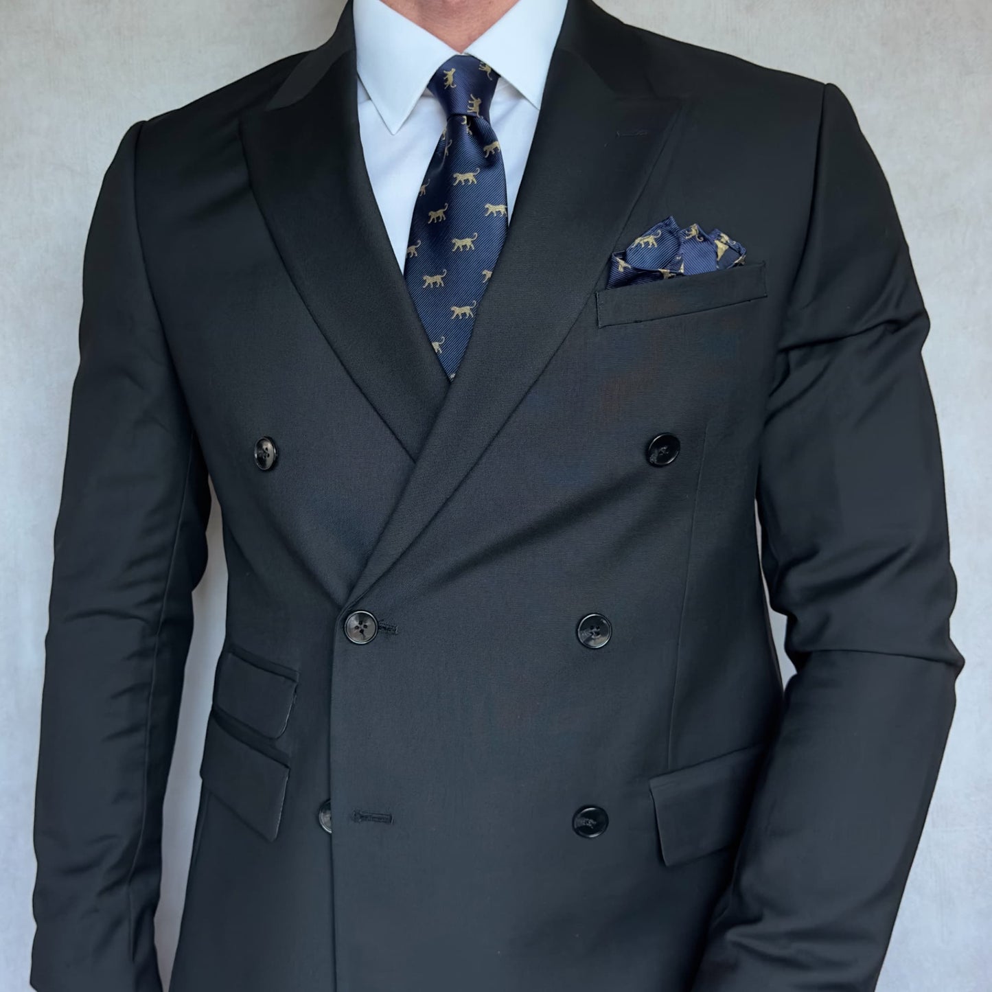 model wearing a black double breasted blazer, white shirt, navy blue necktie with golden silhouettes of a leopard