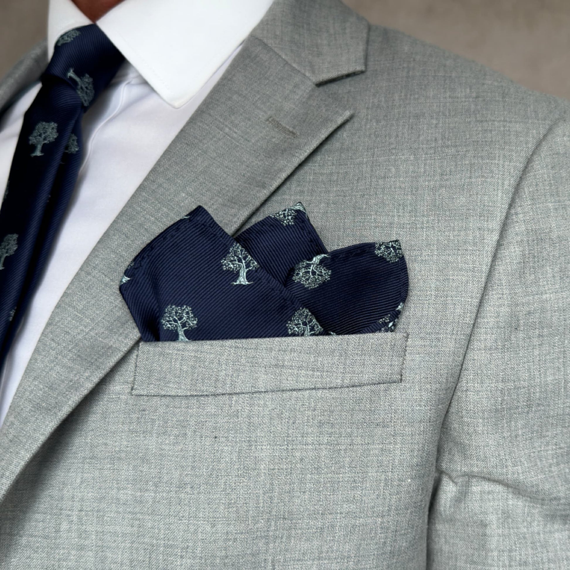 grey pocket highlighting a blue pocket square embroidered with a silver tree pattern