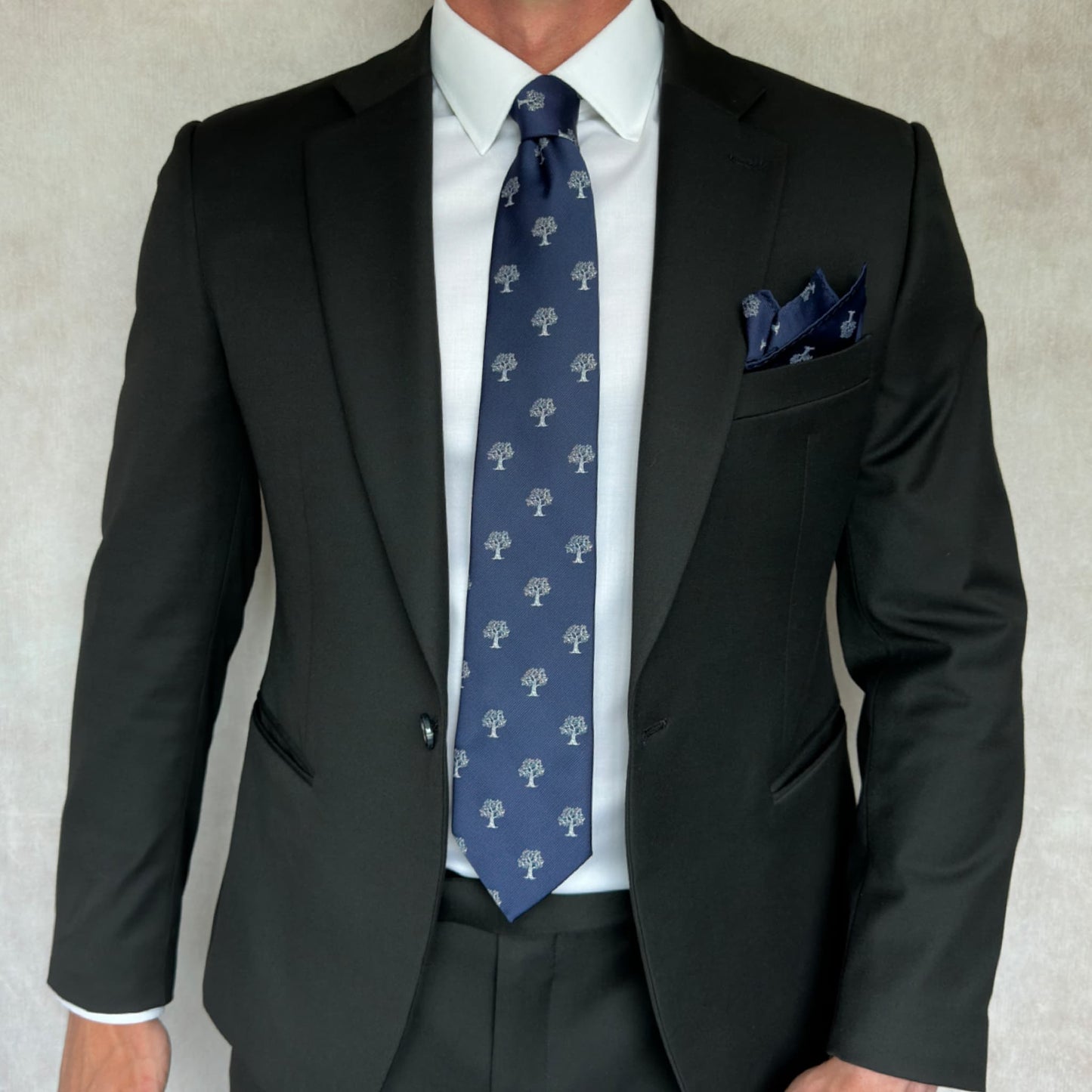 model in black suit shows off blue tie with white tree embroidery