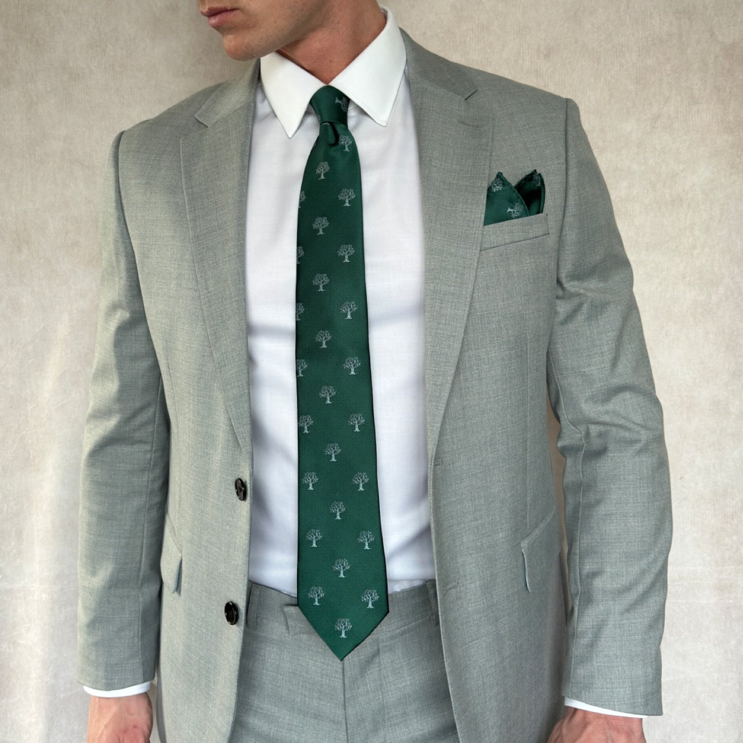 gentleman wearing a grey open suit with matching green and silver tree necktie and pocket square