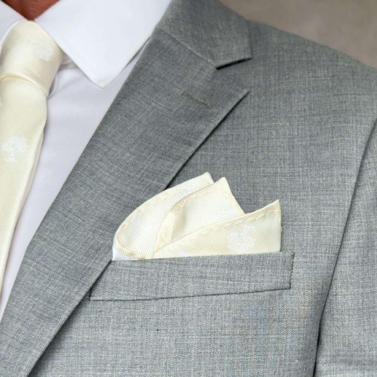 grey suit pocket displaying neatly folded ivory and white pocket square