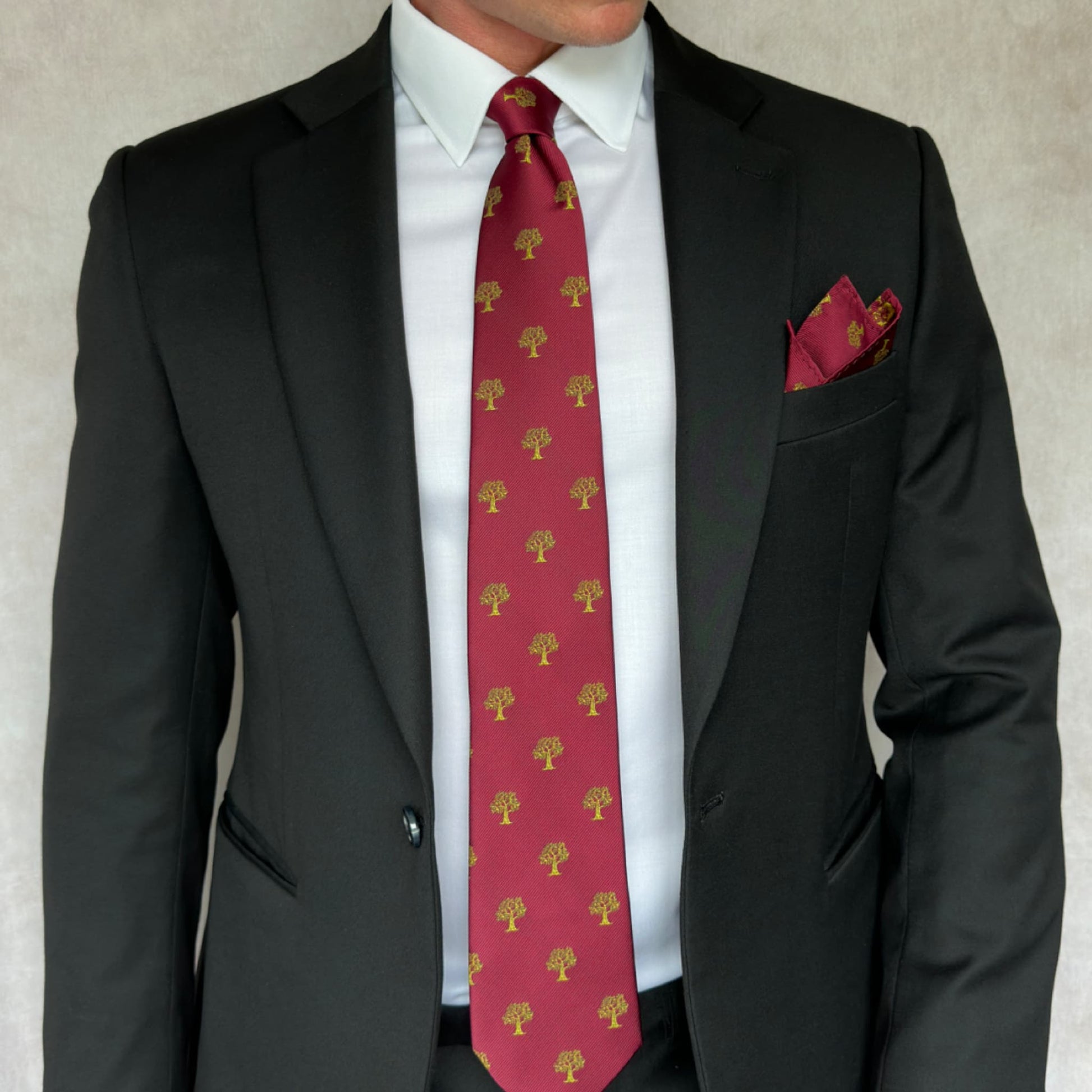 model in a black suit showing off a red necktie printed with golden trees