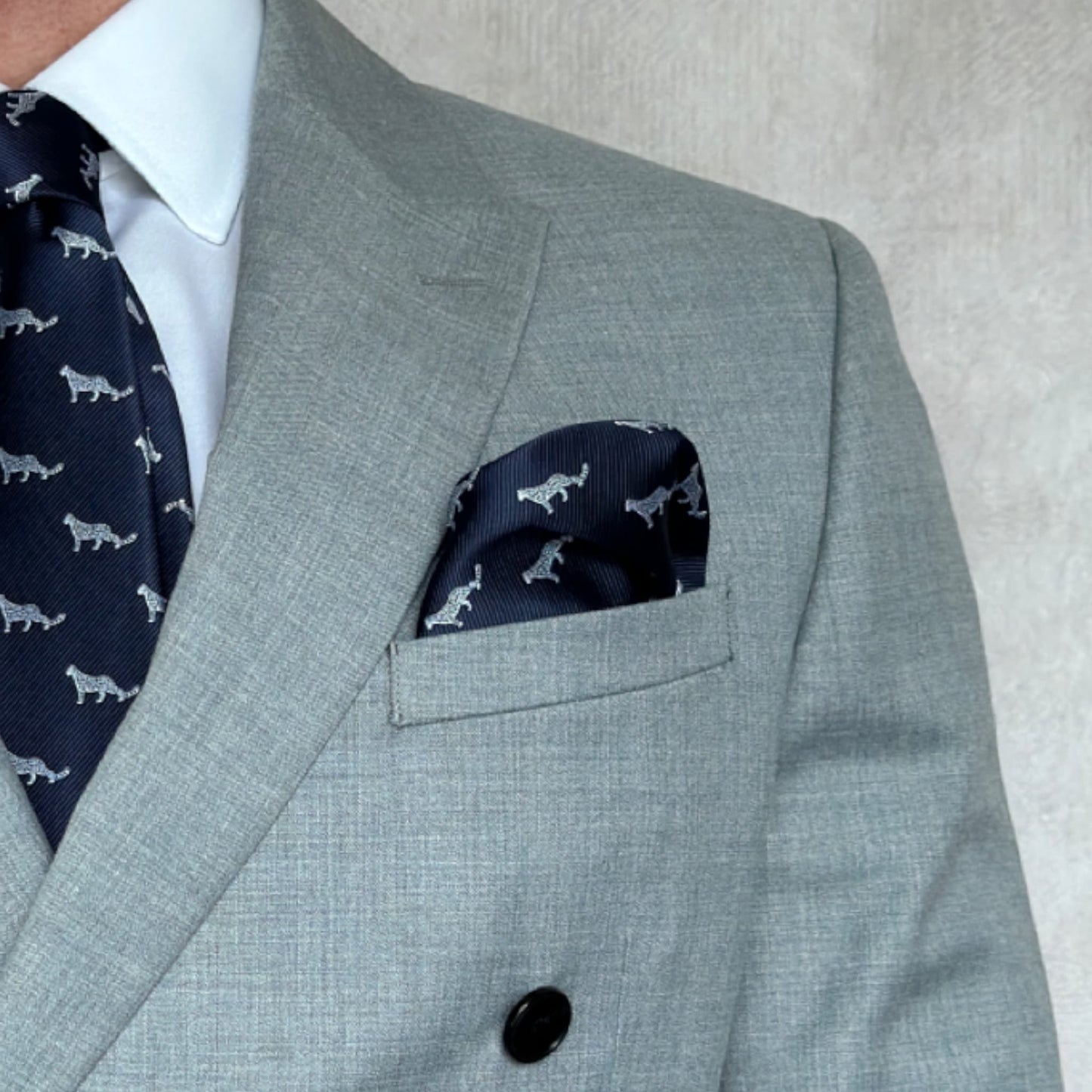 Grey suit pocket highlighting blue pocket square with white snow leopard motif throughout 