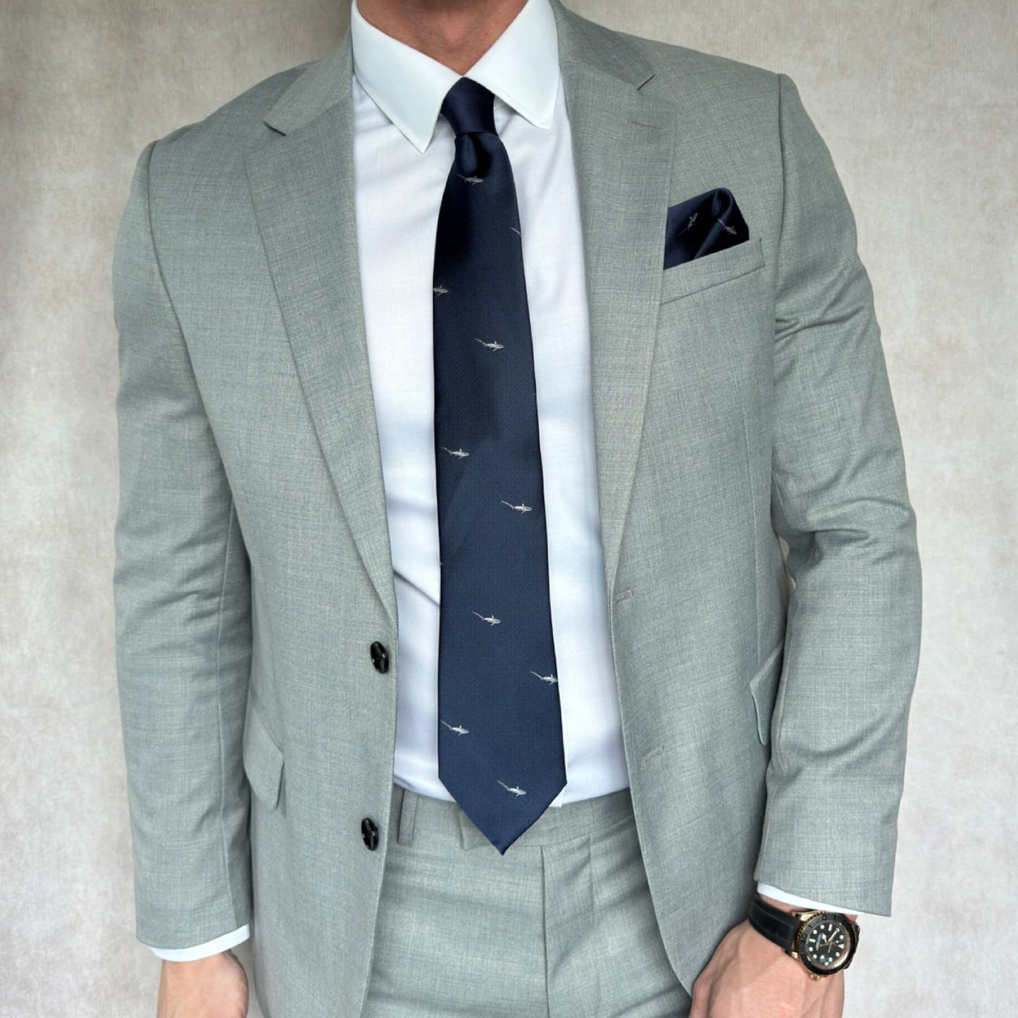 Gentleman wearing a grey open suit and white shirt showing off blue and grey shark embroidered necktie