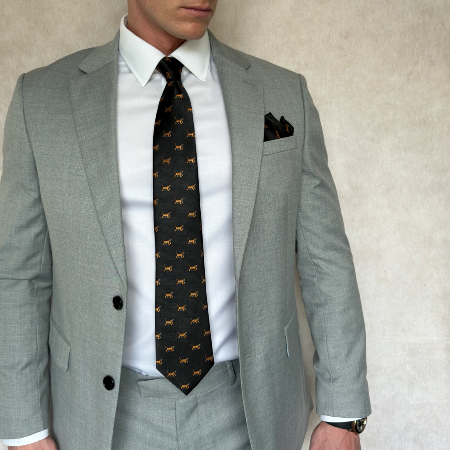 Gentleman in grey suite and white shirt showcasing black tie with tiger embroidery throughout 