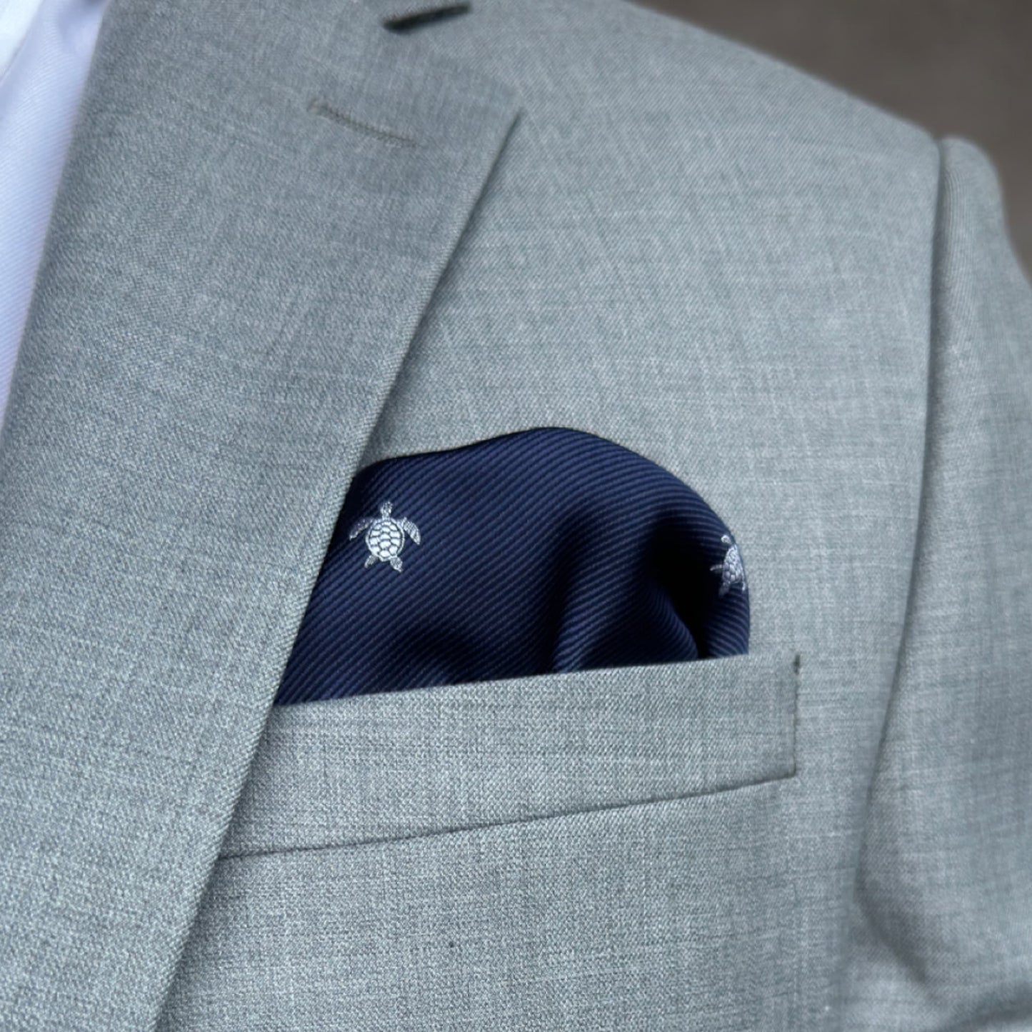 grey suit with blue pocket square showing of intricate silver turtle stitching