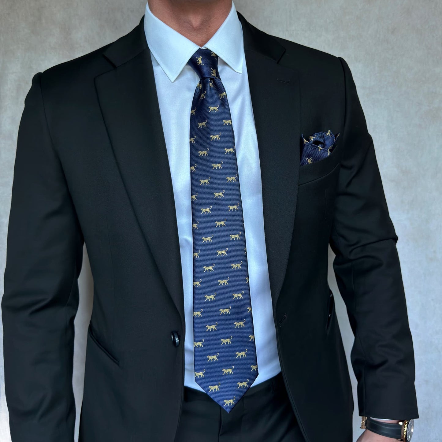 model wearing a black open suit with a navy blue tie that has a gold leopard print throughout 